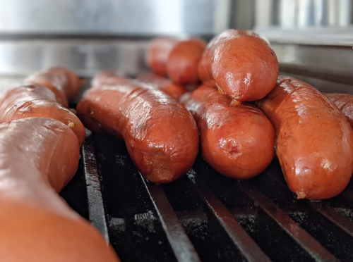 Grilled sausages on a barbecue grill, showcasing a variety of shapes and sizes.