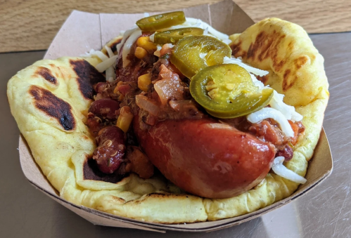 A hot dog topped with chili, jalapeños, and onions, served in a warm flatbread.