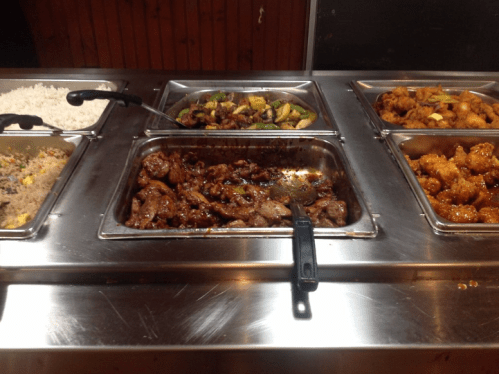 A buffet display featuring various dishes, including rice, vegetables, and meat options in metal trays.