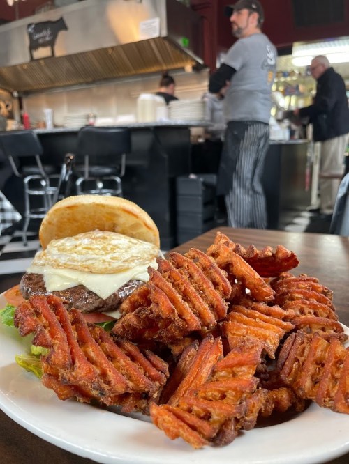 A juicy burger with melted cheese and lettuce, served with crispy waffle fries in a diner setting.