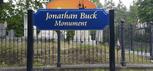 Sign for the Jonathan Buck Monument, with a decorative background and surrounding cemetery.