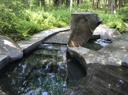 A serene outdoor hot spring surrounded by lush greenery and smooth stone pathways.