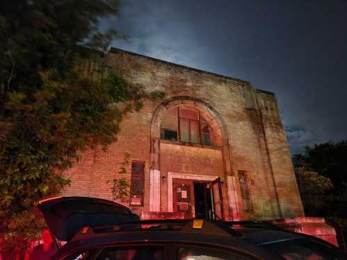 Abandoned building with "Memorial Hospital" sign, illuminated by red light at night, surrounded by trees.