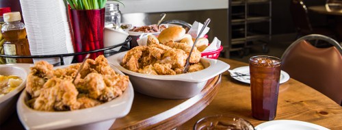 A table set with fried chicken, rolls, sides, and a drink, showcasing a hearty meal in a casual dining setting.