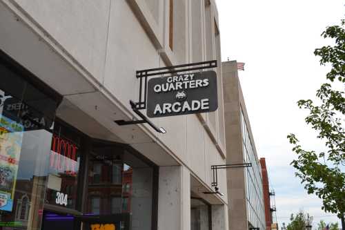 Sign for "Crazy Quarters Arcade" hanging outside a building, with a cloudy sky in the background.