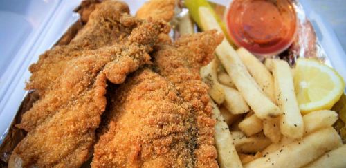 A plate of crispy fried fish fillets with French fries, lemon slices, and a side of dipping sauce.