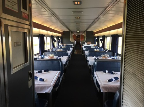Interior of a train dining car with neatly set tables and blue seating, creating a spacious and inviting atmosphere.