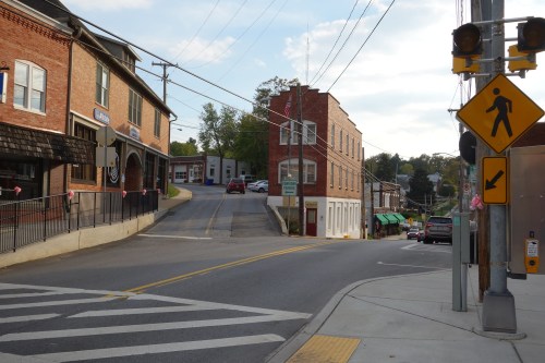 A small town intersection with brick buildings, a crosswalk, and traffic signals under a partly cloudy sky.