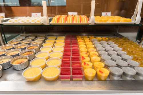 A display of assorted desserts in cups, including mango, jelly, and creamy treats, arranged neatly in a glass case.