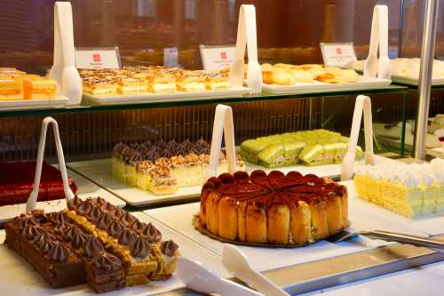 A display of various cakes and pastries, including layered cakes, mousse, and a round tiramisu cake.