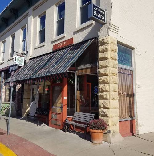 Exterior of La Runa Bistro, featuring a striped awning, wooden benches, and a potted plant by the entrance.