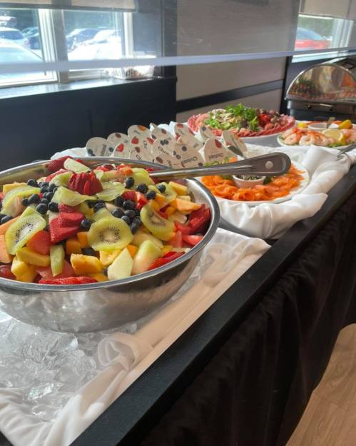 A buffet table featuring a large bowl of mixed fruit salad and various platters of fresh fruits and salads.