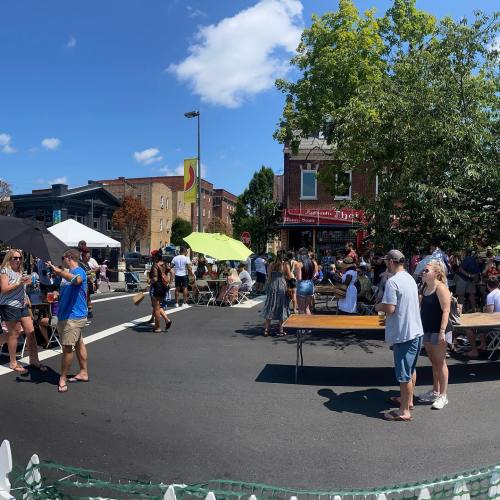 A lively street festival with people sitting at tables, enjoying food and drinks under a clear blue sky.
