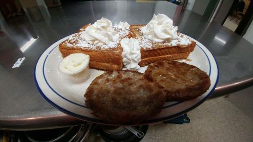 A plate with two pieces of French toast topped with whipped cream and powdered sugar, alongside two sausage patties.