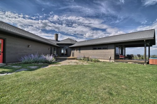 A modern house with a spacious yard, surrounded by greenery and under a blue sky with clouds.
