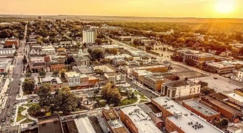 Aerial view of a small town at sunset, showcasing buildings, streets, and a park with trees.