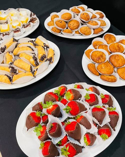 A variety of desserts on white plates, including chocolate-covered strawberries, pastries, and mini muffins.