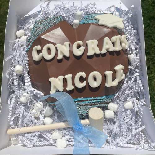 A chocolate gift box with "Congrats Nicole" in white letters, surrounded by marshmallows and a small hammer.