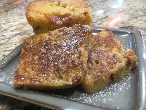 Three pieces of golden cornbread topped with powdered sugar, served on a gray plate against a textured countertop.