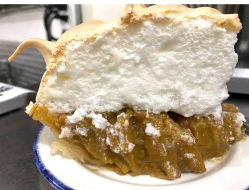 A slice of pie with a golden filling and a fluffy meringue topping on a white plate.