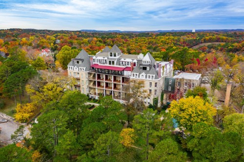 Aerial view of a large, historic building surrounded by vibrant autumn foliage and rolling hills.