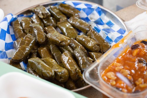 A platter of stuffed grape leaves arranged neatly, with a side of sauce in a container.