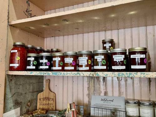 A wooden shelf displaying various jars of homemade jams and preserves, labeled with colorful tags.