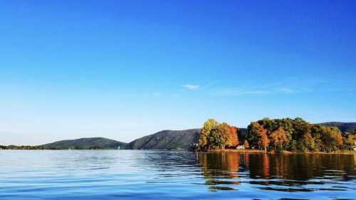 A serene lake scene with calm waters, colorful autumn trees, and distant mountains under a clear blue sky.