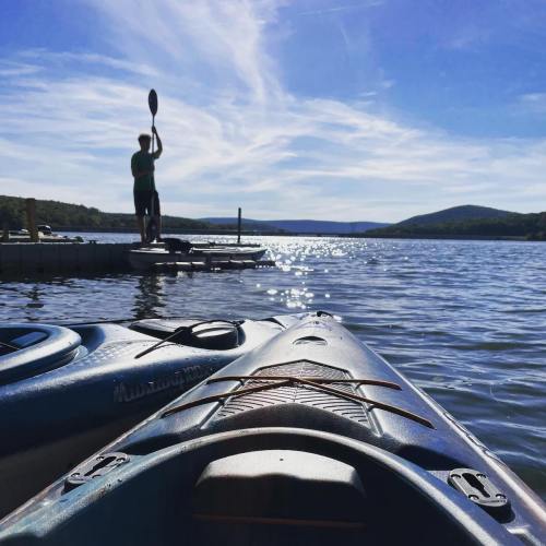 A serene lake scene with kayaks in the foreground and a person paddling in the distance under a blue sky.