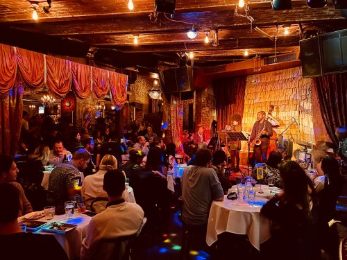 A lively jazz club scene with a band performing on stage, surrounded by an engaged audience at tables.