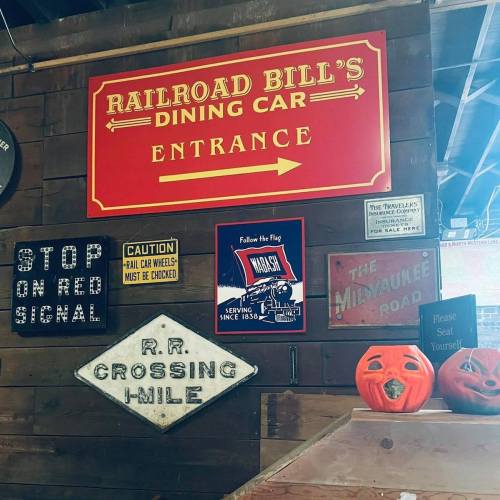 A rustic wall display featuring vintage signs for Railroad Bill's Dining Car, including directional and caution signs.