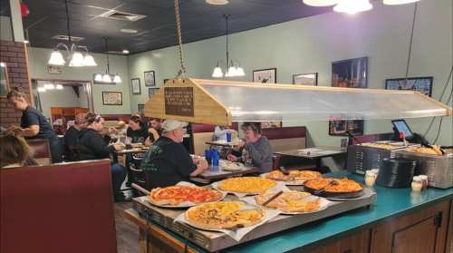 A cozy restaurant interior with diners at booths and a table displaying various pizzas and dishes.