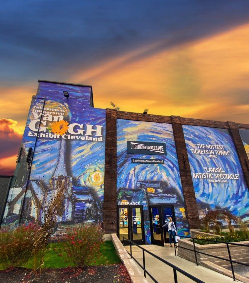 Exterior of the Van Gogh Exhibit in Cleveland, featuring vibrant mural art and a dramatic sunset sky.