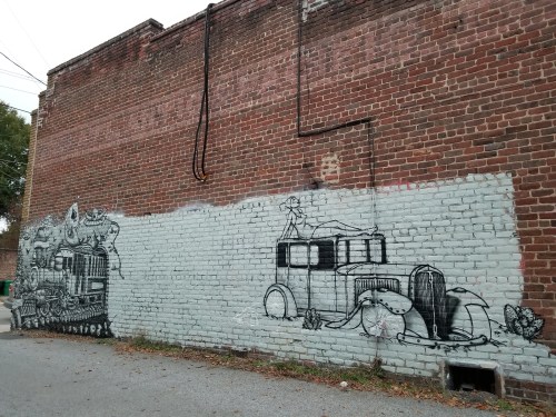 A mural on a brick wall featuring vintage cars and whimsical characters in black and white.