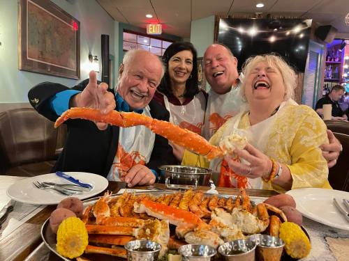 A group of four friends joyfully enjoying a seafood feast, holding a large crab leg and laughing together.