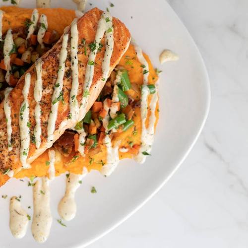 A plate featuring a grilled wrap topped with sauce, served on a bed of colorful vegetables and garnished with herbs.
