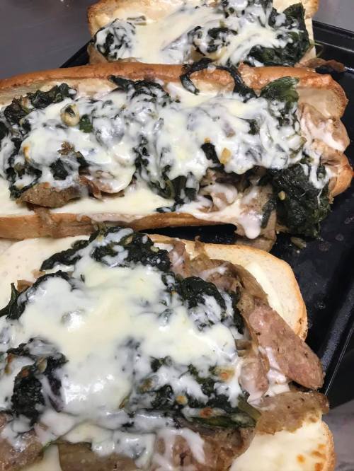 Three toasted sandwich rolls topped with melted cheese, sautéed spinach, and savory meat filling.