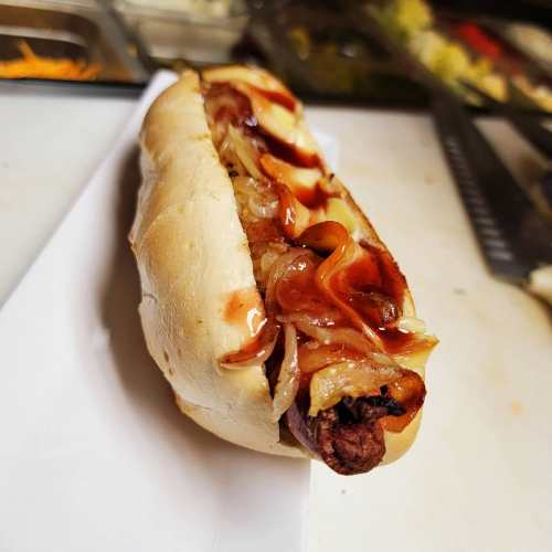 A hot dog in a bun topped with grilled onions and ketchup, served on a white plate.