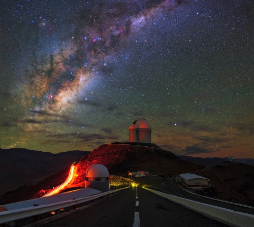 A stunning night sky filled with stars and the Milky Way above an observatory on a mountain road.