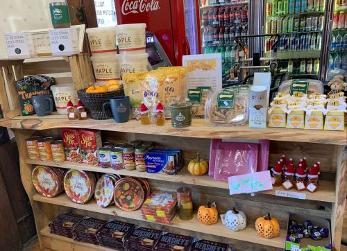 A wooden display shelf filled with various snacks, candies, and maple products, decorated with small pumpkins and festive items.