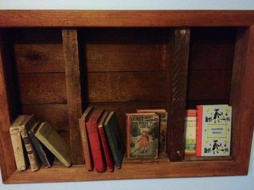 A wooden shelf displaying a collection of vintage books in various colors and sizes.