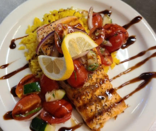 Grilled salmon topped with fresh tomatoes, onions, and lemon, served on a bed of yellow rice with a balsamic drizzle.