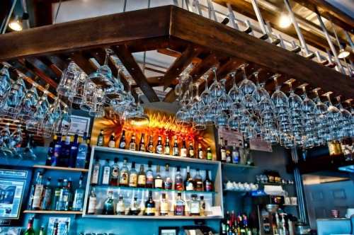 A bar with hanging glassware and a variety of bottles displayed on shelves, illuminated by warm lighting.