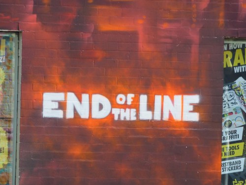 Graffiti on a brick wall reads "END of THE LINE" in bold white letters against a red and orange background.
