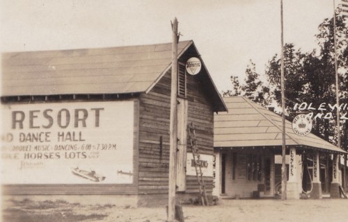 Historic image of a wooden dance hall and resort with signage, surrounded by trees.