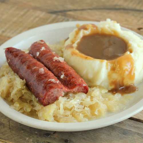 A plate of sausage links served with mashed potatoes and gravy, alongside a portion of sauerkraut.