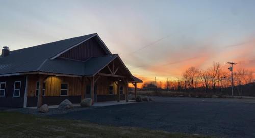 A rustic building at sunset, with a colorful sky and trees in the background, surrounded by gravel and boulders.