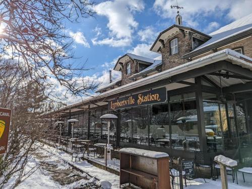 Historic restaurant with outdoor seating, surrounded by snow, under a bright blue sky with scattered clouds.