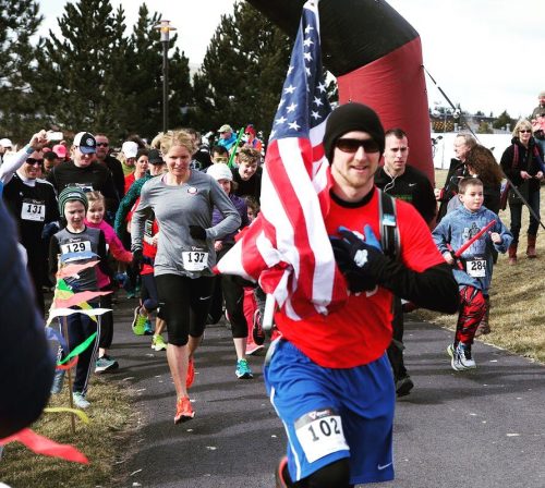 A group of runners, including one holding an American flag, participating in a race on a cool day.