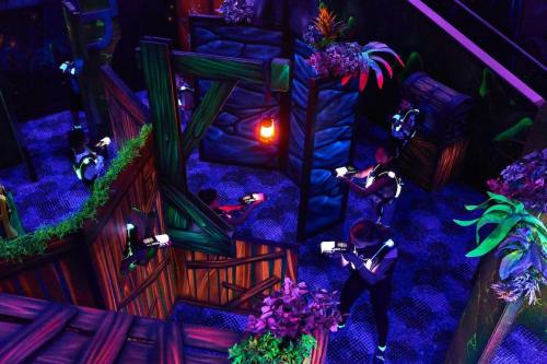 A vibrant indoor laser tag arena with players navigating through colorful obstacles and glowing plants.